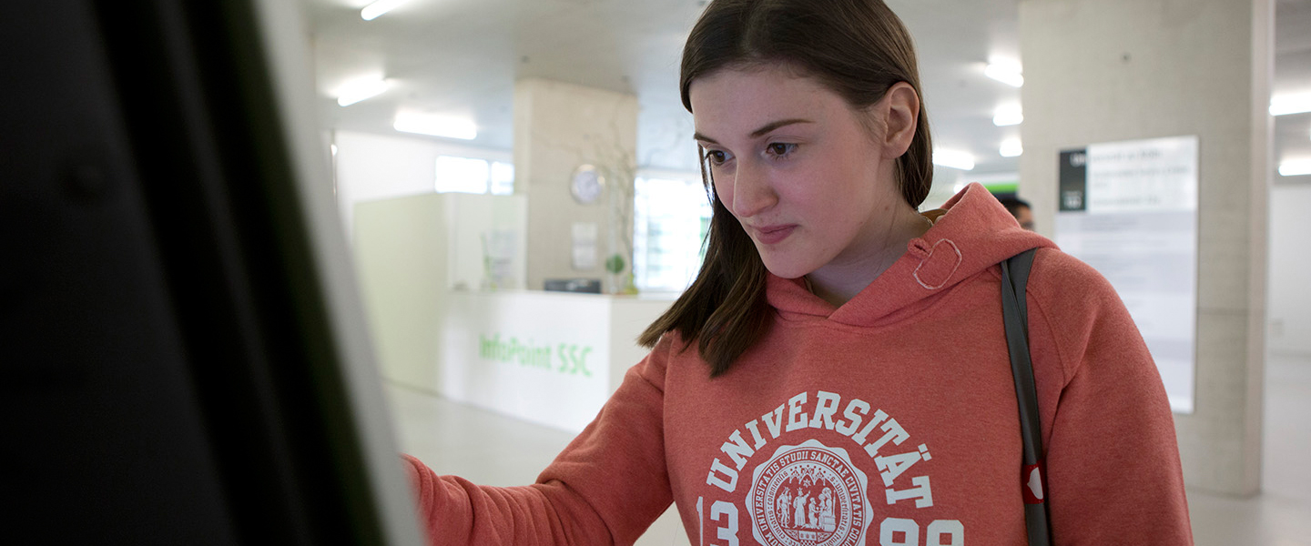 Studentin trägt Hoodie mit Universitäts-Logo und informiert sich an Whiteboard. 