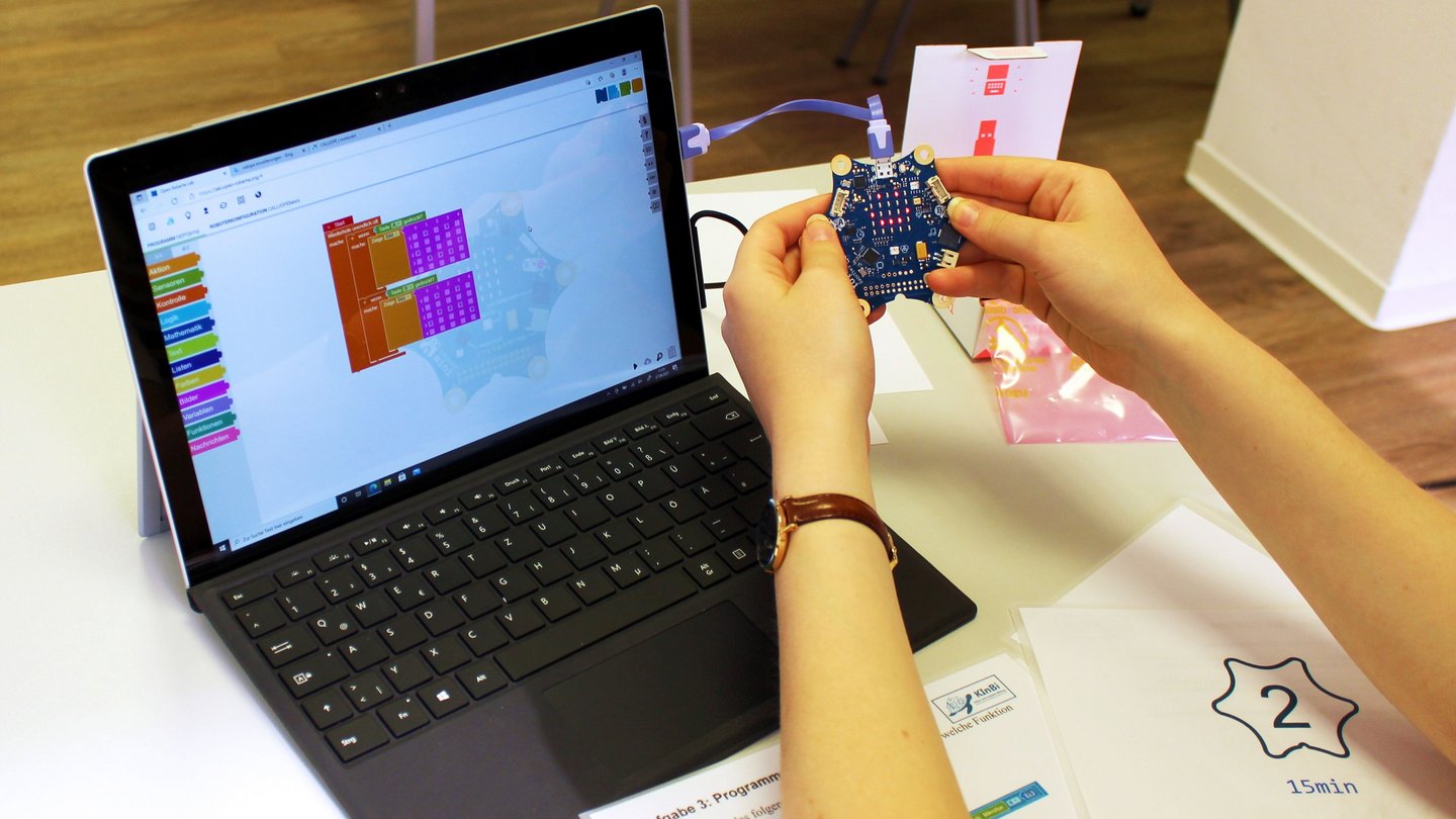 Ein Laptop mit geöffnetem Programm im Open Roberta Lab ist zu sehen. Daran angeschlossen ist ein Calliope mini Roboter, dessen LED Anzeige einen lachenden Smiley zeigt.